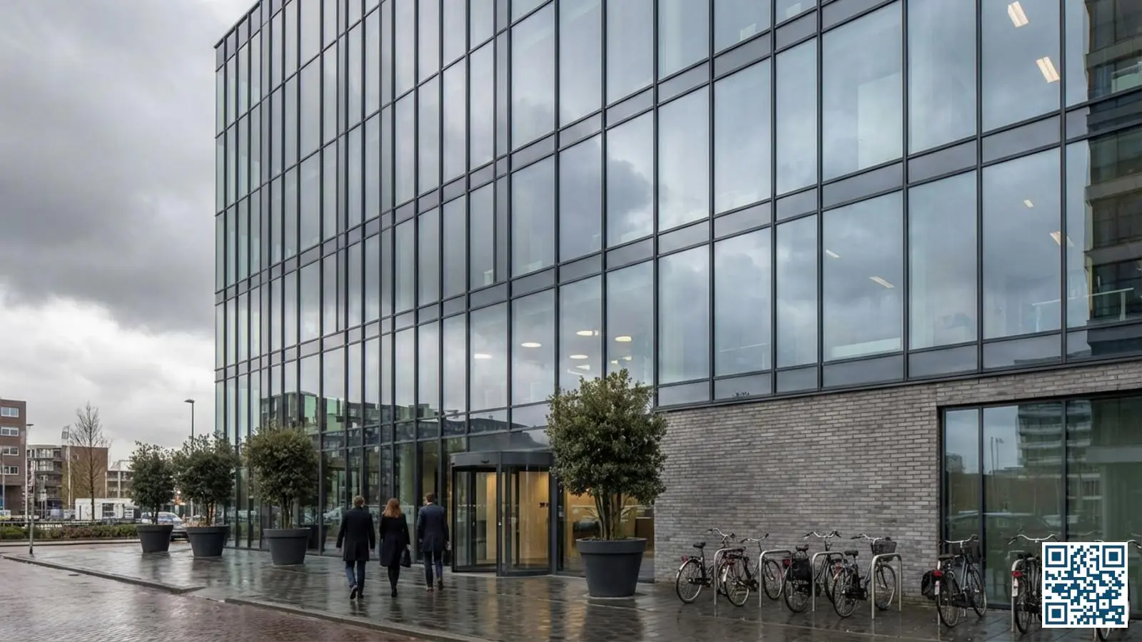 Modern kantoorgebouw met grote glazen gevelpartijen die de bewolkte lucht reflecteren in een stedelijke omgeving